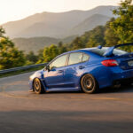 Subaru WRX bleue en plein virage sur une route de montagne sinueuse au coucher du soleil, avec un effet de mouvement dynamique.