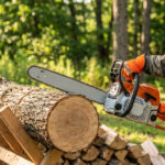 Homme en tenue de sécurité coupant une bûche de bois avec une tronçonneuse sur un chevalet de sciage. Des bûches empilées à l'arrière.